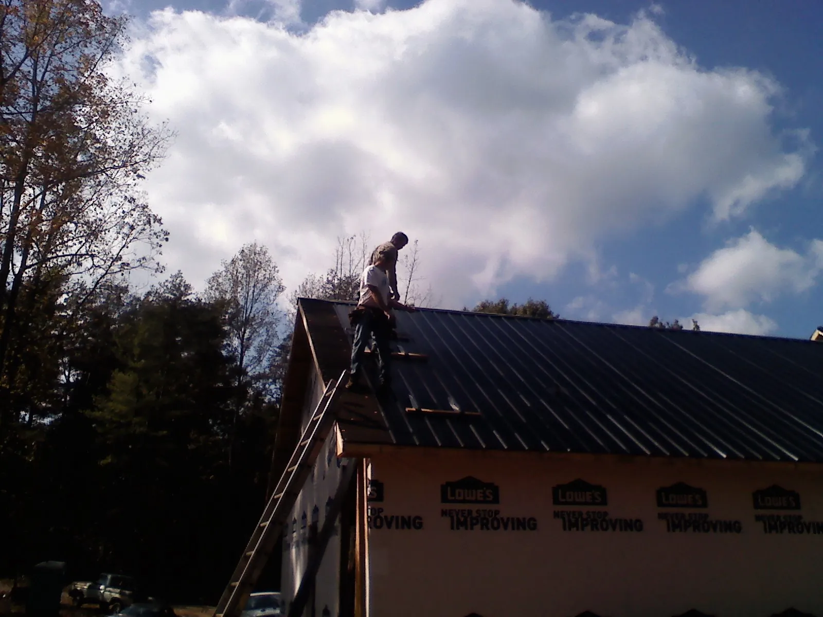 Roofer fastening dark metal panels high against a cloudy sky, from a Roof Inspection job in Glenn Dale