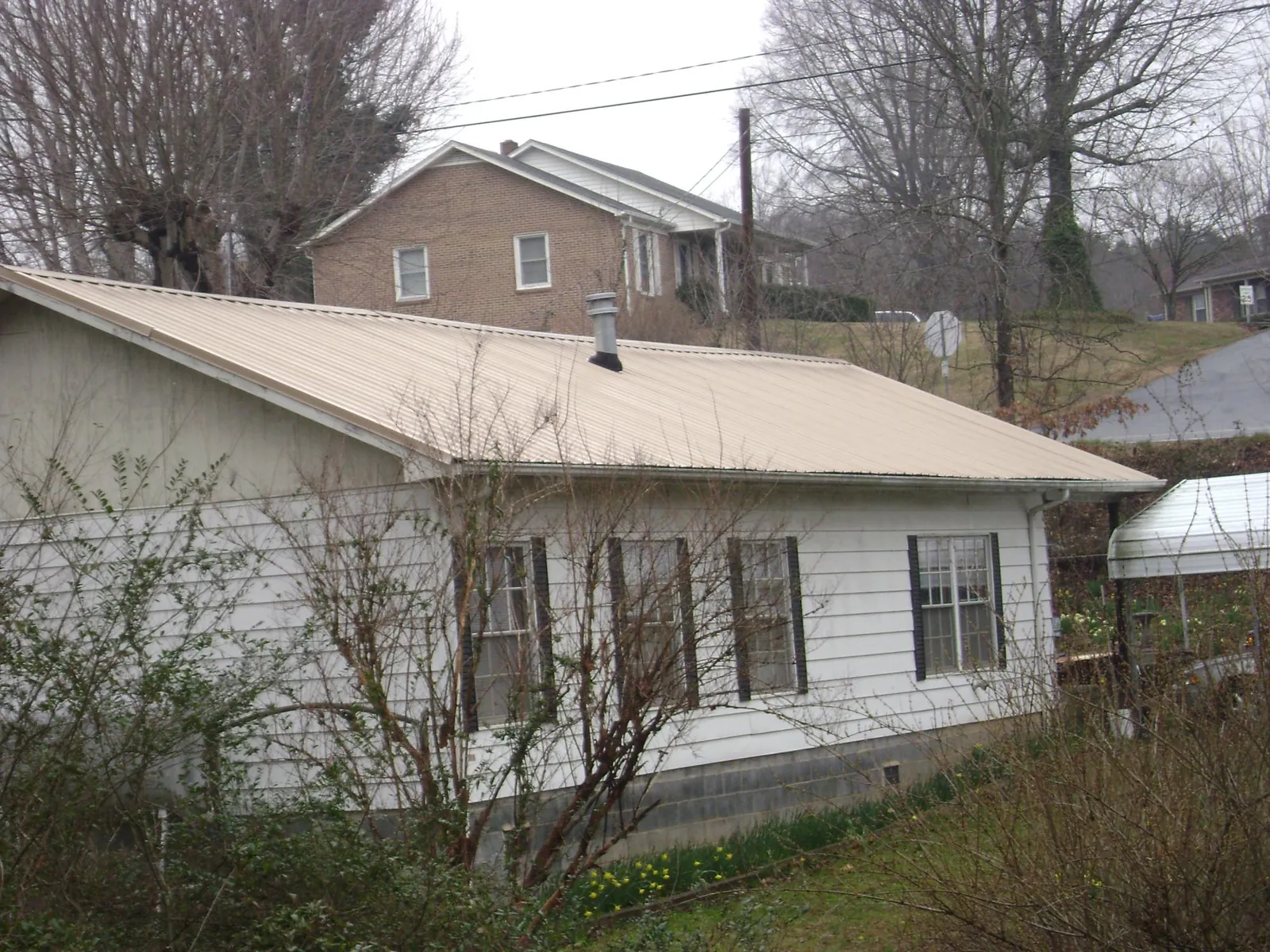 Tan metal roof on a white sided house set into a hillside — Commercial Roofing by Roofing Brothers in Glenn Dale