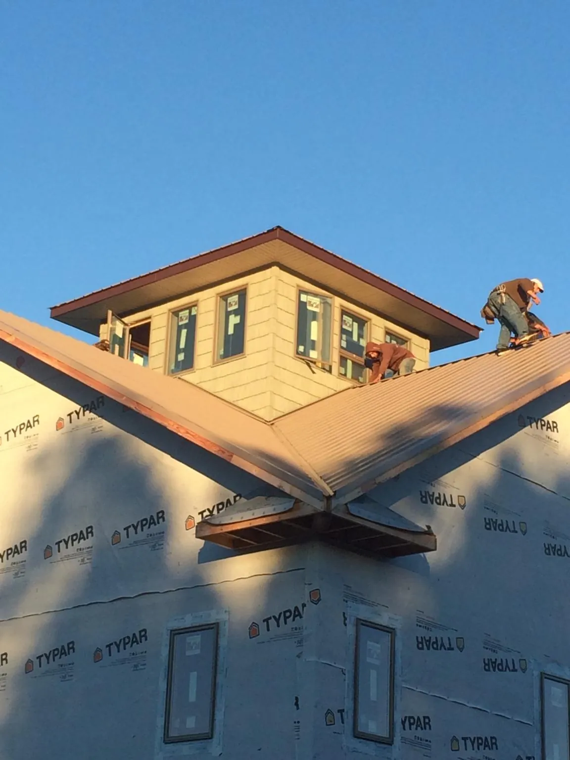 Roofers working around a rooftop cupola on a new metal roof at sunset — Roof Waterproofing in Glenn Dale by Roofing Brothers